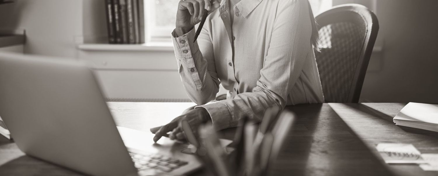 Eine weiblich gelesene Person sitzt am Schreibtisch mit Laptop